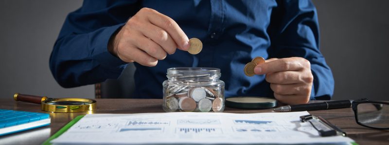 Businessman putting coin in glass bank. Saving money